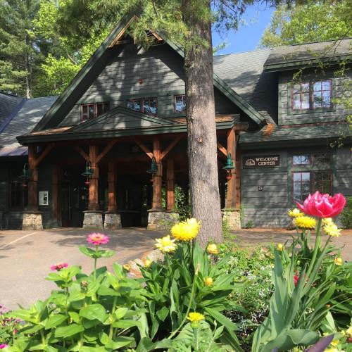 A welcoming lodge surrounded by colorful flowers and trees on a sunny day.