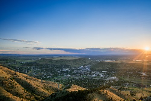 A panoramic view of a valley at sunset, with rolling hills and a small town nestled below under a colorful sky.