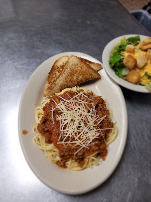 A plate of spaghetti topped with meat sauce and grated cheese, served with toasted bread and a side salad.