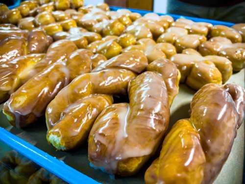 A tray of freshly glazed donuts in various shapes, showcasing a shiny, sweet icing on top.