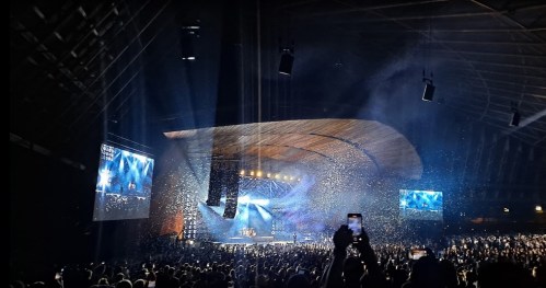 A lively concert scene with a large crowd, colorful lights, and confetti falling from the stage.