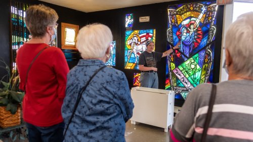 A guide explains stained glass art to a small group of attentive visitors in a brightly lit room.