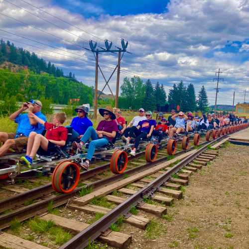 A group of people riding on a rail bike along train tracks, surrounded by trees and a cloudy sky.