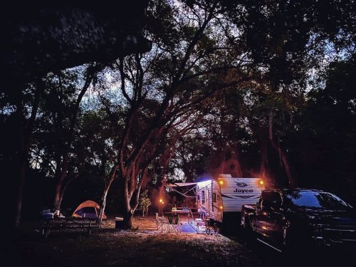 A cozy campsite at dusk featuring a Jayco RV, a tent, and warm lights among trees.