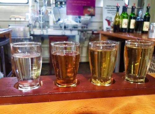 Four glasses of different beverages on a wooden tray, set against a bar with bottles in the background.