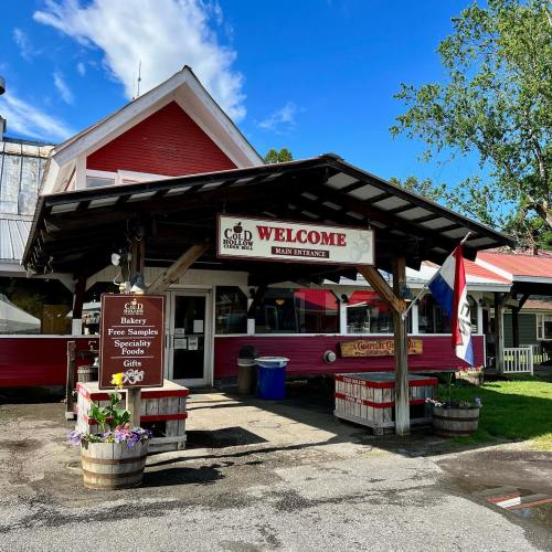 A welcoming entrance to a bakery with signs for free samples and specialty foods, surrounded by greenery.