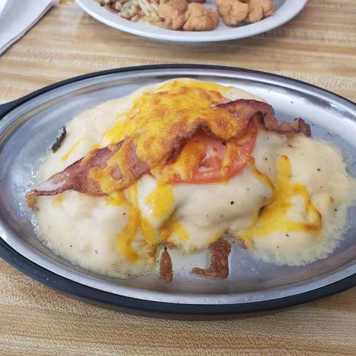 A sizzling plate of creamy cheese sauce topped with bacon and tomato, served over a bed of fluffy mashed potatoes.
