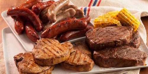 A platter of grilled meats including sausages and steaks, accompanied by corn on the cob.