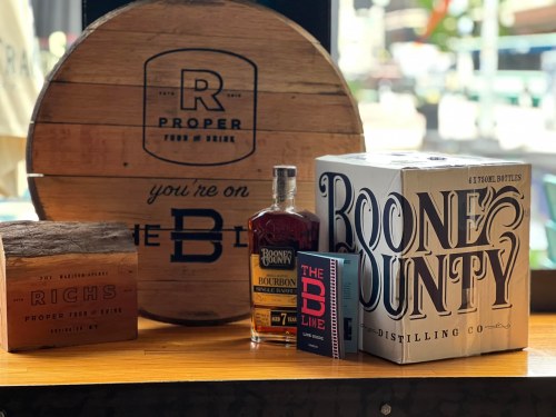 A display featuring Boone County bourbon, a wooden barrel, and branded merchandise on a wooden table.