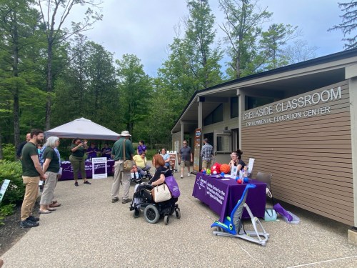 A group of people at an outdoor event near a building, with tables displaying information and activities.