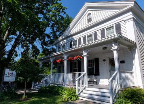 A charming white house with a porch, flower boxes, and a sign for Houghton Gallery, surrounded by greenery.