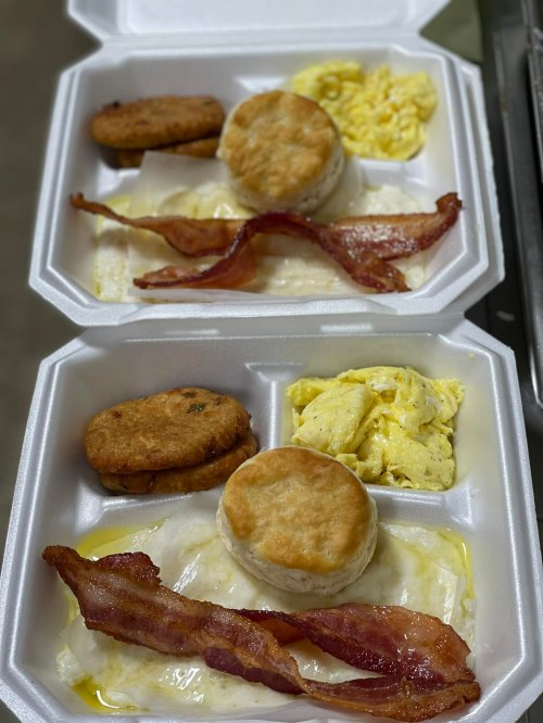 Two takeout containers with biscuits, scrambled eggs, bacon, and sausage patties.