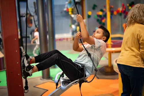 A child plays on a climbing apparatus in a colorful indoor playground, focused and engaged in the activity.
