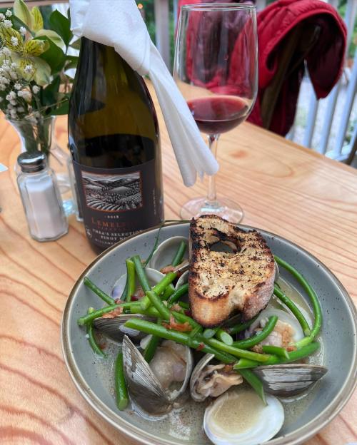 A plate of seafood with green beans and grilled bread, accompanied by a bottle of wine and a glass on a wooden table.