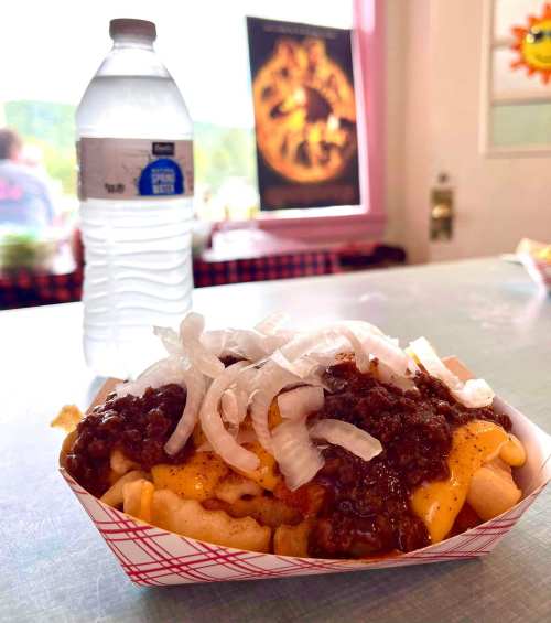 A tray of chili cheese fries topped with onions, next to a bottle of water, in a casual dining setting.