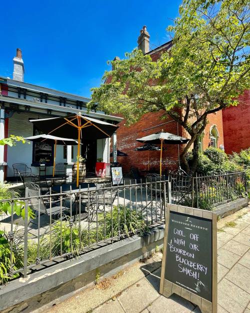 A sunny outdoor seating area of a restaurant with umbrellas and a sign promoting a Bourbon Blackberry Smash.