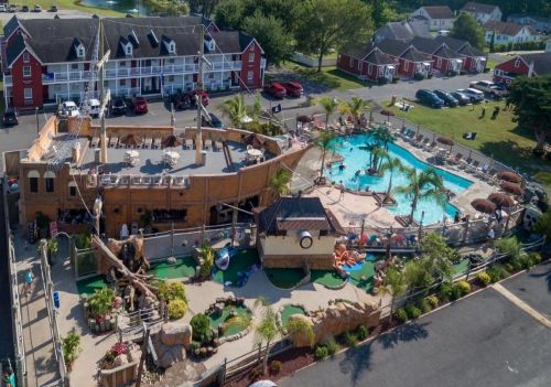 Aerial view of a resort featuring a pirate ship pool, mini-golf, and tropical landscaping surrounded by colorful buildings.