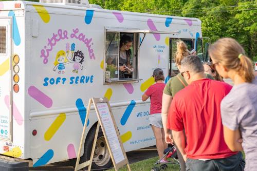 A colorful ice cream truck with a line of customers waiting to order soft serve treats.