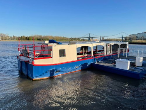 A colorful boat docked on calm water, with a bridge visible in the background under a clear blue sky.