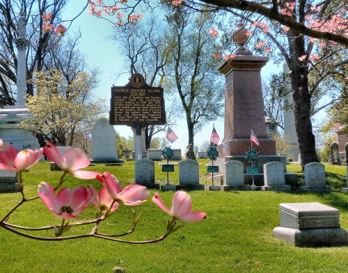 A peaceful cemetery scene with a historical marker, gravestones, and blooming flowers in the foreground.