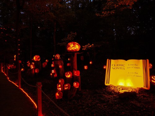 A dark forest path lined with glowing jack-o'-lanterns and a sign featuring a classic novel quote.