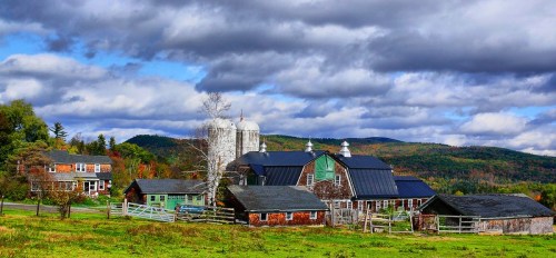 A picturesque farm scene with barns, silos, and rolling hills under a cloudy sky, showcasing autumn colors.