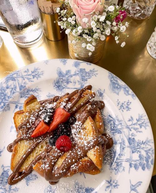 A plate of French toast topped with chocolate spread, strawberries, and berries, beside a small flower arrangement.