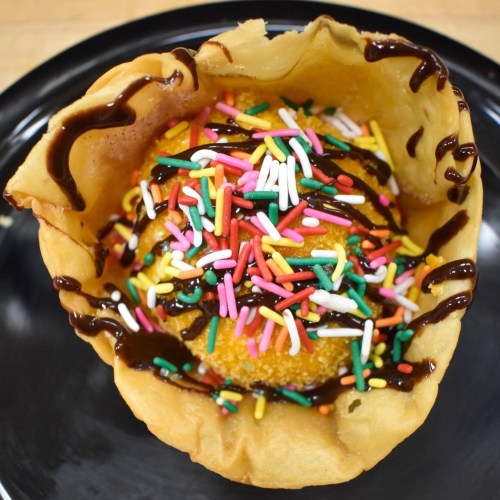 A dessert in a waffle bowl, featuring ice cream topped with chocolate sauce and colorful sprinkles.