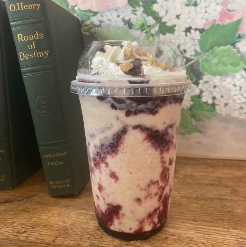 A creamy drink with swirls of berry sauce, topped with whipped cream and crumbs, beside a book titled "Roads of Destiny."