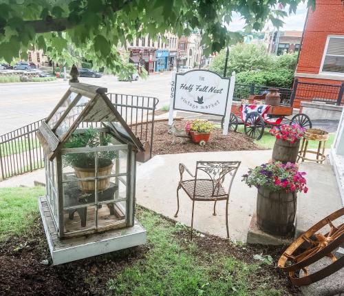 A quaint outdoor market scene featuring a greenhouse, flower pots, and rustic seating near a street.