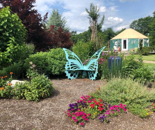 A large blue butterfly sculpture surrounded by colorful flowers and greenery, with a tent-like structure in the background.