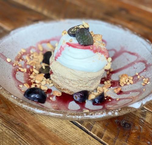 A dessert featuring a creamy layer topped with whipped cream, nuts, and dark berries on a rustic plate.