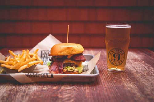 A delicious burger with bacon and lettuce, served with fries and a pint of beer on a wooden table.