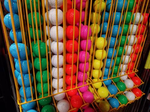 A colorful display of golf balls in a wire rack, featuring blue, white, pink, orange, and yellow balls.