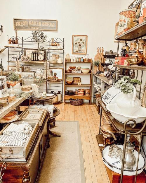 A cozy shop interior filled with vintage kitchenware, baked goods, and rustic decor on wooden shelves.