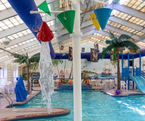 Indoor pool area with colorful water features, palm trees, and a slide, creating a fun, tropical atmosphere.