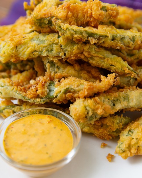 A close-up of crispy fried green beans served with a small bowl of dipping sauce.