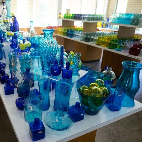 A display of various blue and green glass vases and bottles arranged on tables in a bright, airy space.