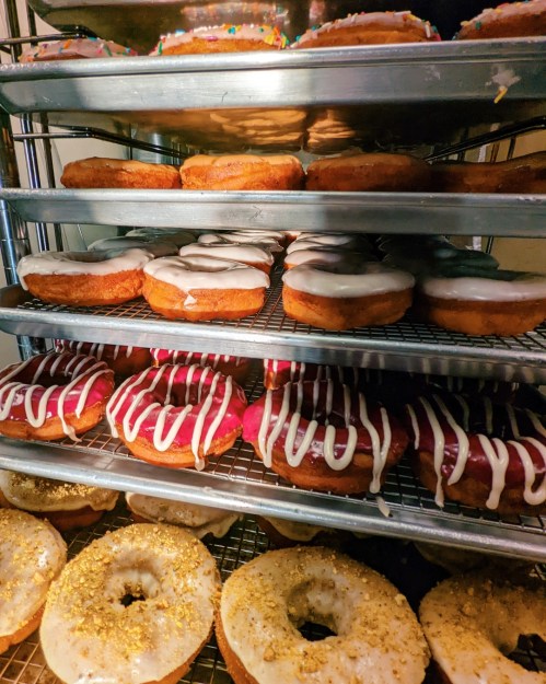 A display of assorted donuts on wire racks, featuring various glazes and toppings in vibrant colors.