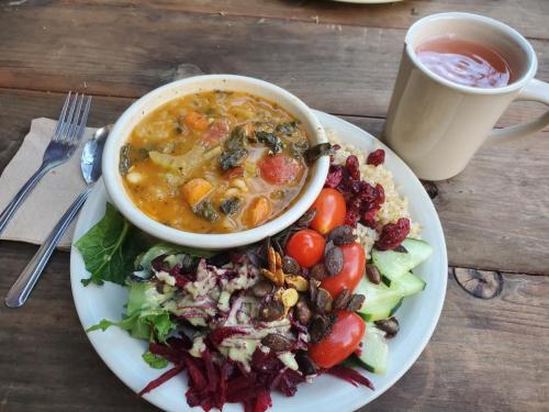 A bowl of vegetable soup with a side salad of tomatoes, cucumbers, and beets, accompanied by a cup of tea.