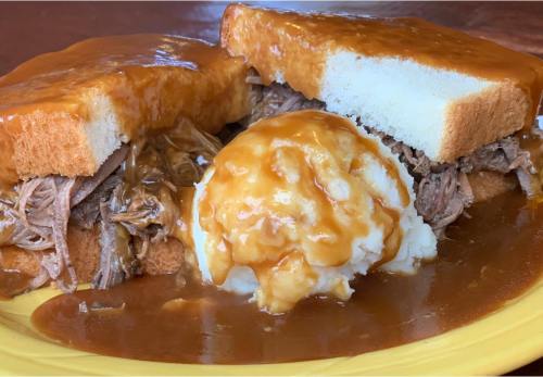 A plate featuring shredded beef on bread, topped with gravy, alongside a scoop of mashed potatoes with gravy.