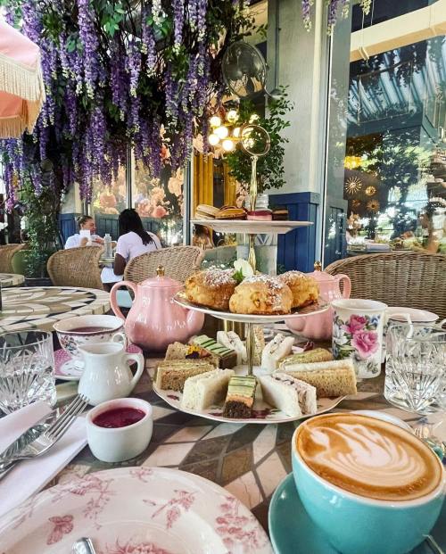 A beautifully arranged afternoon tea set with pastries, sandwiches, and drinks, surrounded by floral decor.