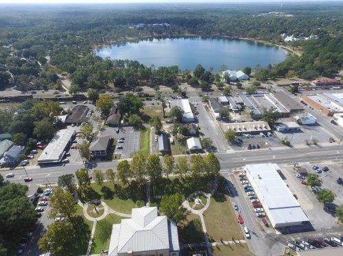 Aerial view of a town with a lake, surrounded by trees and buildings, showcasing streets and parked cars.