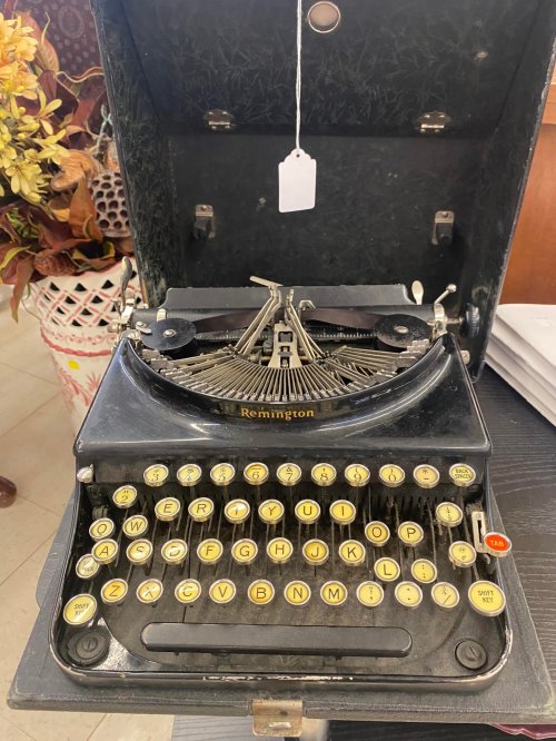 A vintage Remington typewriter with a black exterior and yellow keys, displayed with a tag hanging from the top.