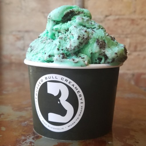 A cup of mint chocolate chip ice cream with cookie crumbles, served in a black container with a bull logo.
