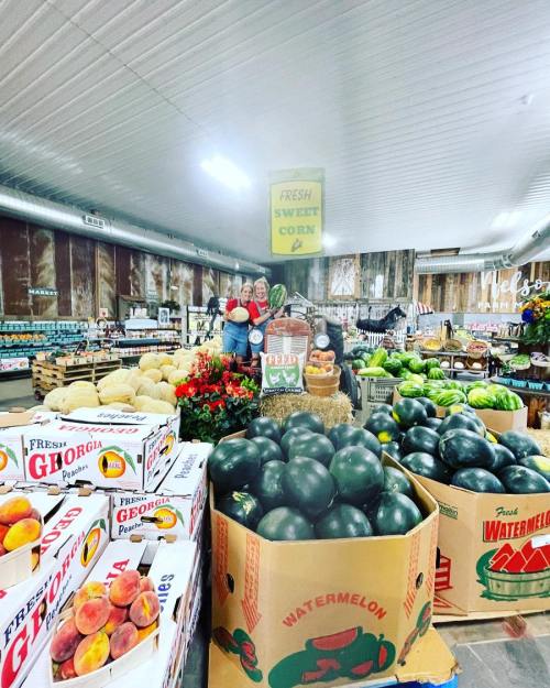 A vibrant market display featuring watermelons, peaches, and fresh corn, with colorful produce and cheerful decorations.