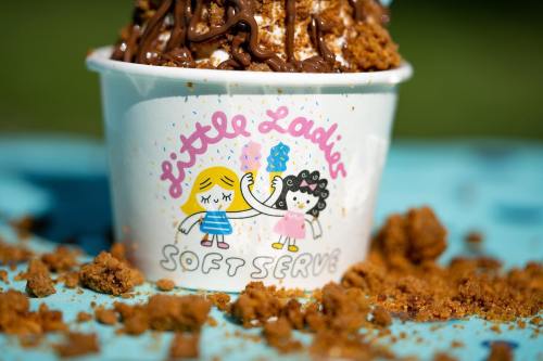 A cup of soft serve ice cream topped with chocolate drizzle and crumbs, featuring a playful cartoon design.