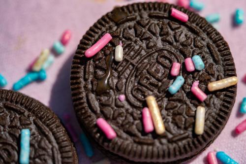 Close-up of an Oreo cookie topped with colorful sprinkles on a pink background.