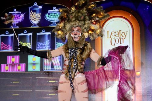 A performer in a lion costume with a dramatic headdress and a pink tulle skirt, posing on stage at LeakyCon.