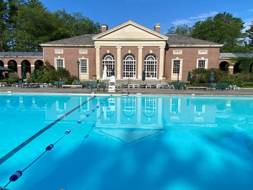A serene pool area with a brick building in the background, surrounded by greenery and clear blue skies.